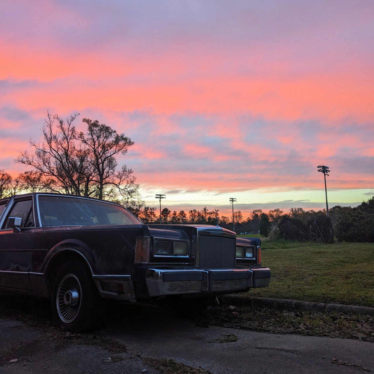 The old Lincoln, a relic of forgotten grandeur, stands sentinel under a sky bruised with the colors of a dying day.
